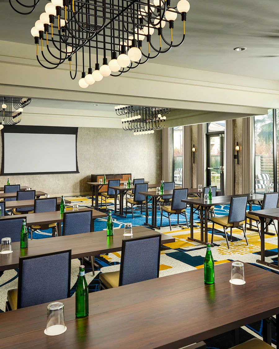 Meeting room set classroom-style with water bottles, a projection screen, globe-bulb chandeliers, and colorful carpet