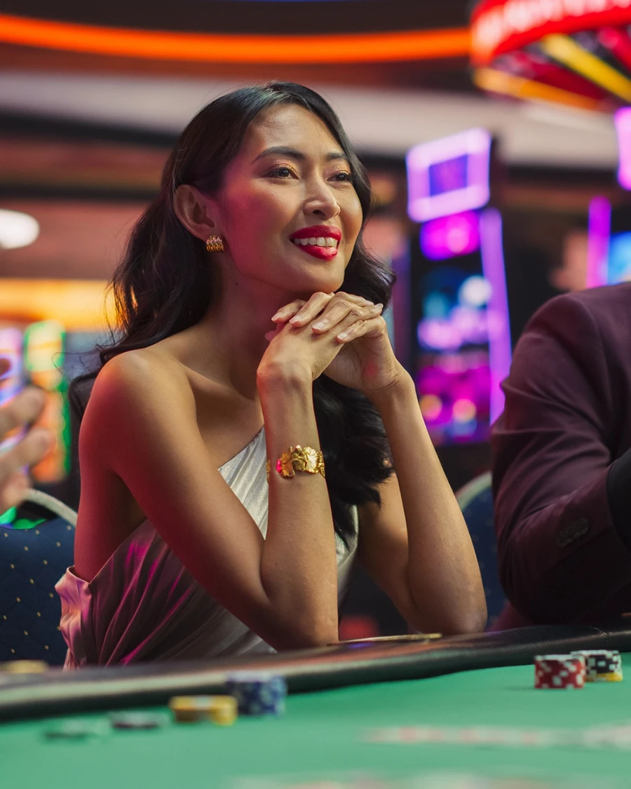 Smiling woman in a white dress sits at a casino table with poker chips, neon slot machines glowing behind her
