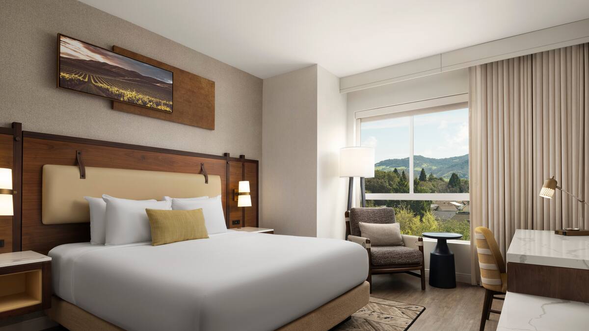 Hotel Centro king bedroom with vineyard artwork, armchair, desk, and a window overlooking green Sonoma hills