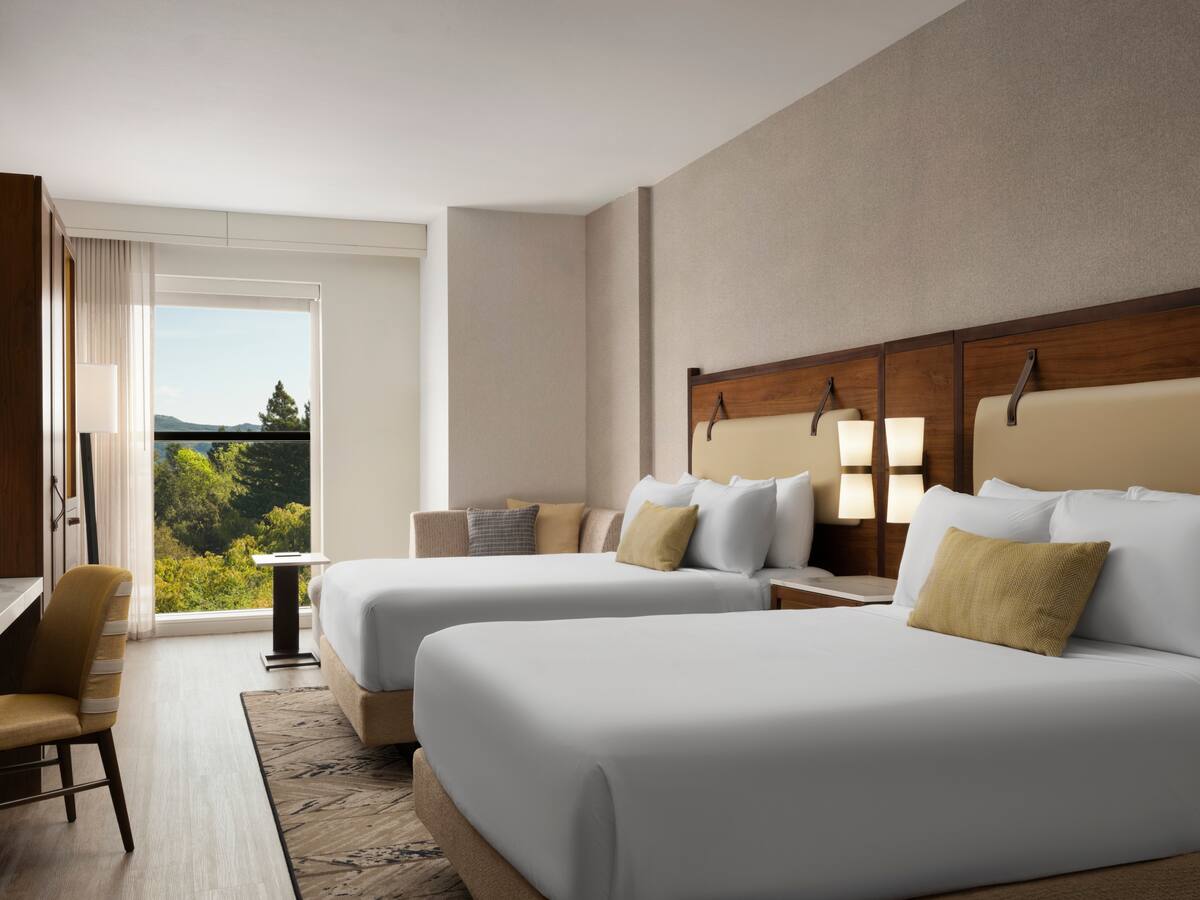 Hotel Centro guest room with two queen beds, wood headboards, a sofa, and a large window overlooking green trees and hills